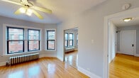 This single-floor residence offers a thoughtfully laid-out interior that balances classic architectural character with practical functionality. Warm, polished hardwood floors extend throughout the living areas, bedrooms, and hallway, lending a cohesive and inviting feel to the entire space. A central hallway, lit by a brass-toned flush-mount ceiling fixture, connects the rooms with an elegant simplicity, featuring crisp white trim and neutral gray walls.

The spacious main living area is anchored by a distinctive bay window arrangement, offering generous natural light and views of the surrounding brick streetscape. A ceiling fan overhead and a cast-iron radiator beneath the windows reflect the unit's blend of period detail and comfort. Mirrored sliding closet doors enhance the sense of openness in this room.

The bedrooms are well-proportioned, each featuring ceiling fans, hardwood floors, and large windows that invite natural light. Cast-iron radiators provide classic, reliable heating throughout.

The kitchen is equipped with light maple cabinetry, granite-style countertops, a stainless steel sink, gas range, dishwasher, microwave, and refrigerator — providing ample storage and modern appliances for everyday living.

The bathroom is finished with white tile surrounding a full tub and shower, complemented by a window for natural ventilation and a mirrored vanity for added practicality.