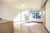 Located at 300 E Grand Ave in Des Moines, Iowa, this efficiently designed single-floor unit offers a well-organized layout that maximizes every square foot. The open-concept kitchen and living area serves as the heart of the space, featuring warm wood-toned cabinetry, a full suite of stainless steel appliances — including a refrigerator, electric range, built-in microwave, and dishwasher — and a peninsula counter that provides additional prep and dining space. Light-toned hardwood flooring runs throughout the kitchen and living area, lending a clean, contemporary feel. Large sliding glass doors in the living area open to a private balcony, flooding the space with natural light and offering views of the surrounding urban streetscape. A separate bedroom features plush carpeting, a generous closet with sliding wood-panel doors, and a window with a tree-lined outdoor view. In-unit laundry with a stacked washer and dryer is conveniently tucked alongside the bedroom. The bathroom, utility room, and additional closet storage round out the functional layout. Exposed ductwork visible in the kitchen area adds an industrial design accent, complementing the modern, no-fuss aesthetic found throughout the unit.