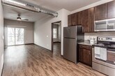 This contemporary single-floor unit blends modern design with industrial-chic details throughout. A defining architectural feature is the exposed silver ductwork that runs prominently through the main living and kitchen areas, adding an urban loft character to the space. Rich, warm hardwood-style flooring extends seamlessly throughout every room, creating a cohesive and inviting atmosphere.

The kitchen is well-appointed with dark espresso cabinetry reaching toward the ceiling, providing ample storage. A full suite of stainless steel appliances — including a refrigerator, range, microwave, and dishwasher — offers both style and functionality. Recessed lighting illuminates the kitchen workspace, complemented by under-cabinet lighting over the countertops.

The open living area flows directly from the kitchen and is bathed in natural light from a large sliding glass door that opens to a private balcony with outdoor views of surrounding trees. A ceiling fan adds comfort to this generously sized gathering space.

The bedroom is a calm, well-lit retreat featuring multiple windows, a ceiling fan, and direct access to the bathroom. The bathroom includes a dark-cabinetry vanity with an integrated sink, a shower with curtain, and hardwood-style flooring that continues from the adjacent rooms. A walk-in closet area provides practical storage solutions.