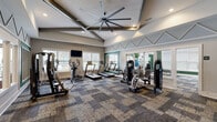 Located at 195 N Creek Dr in Summerville, SC, this single-story clubhouse showcases refined interior design with a welcoming and upscale atmosphere. The entry foyer makes an immediate impression with soaring double-height ceilings, a striking blue accent ceiling detail, decorative pendant lighting, and large-format light tile flooring. A grand arched transom window above the front door floods the entry with natural light, complemented by warm wood-accent wall paneling and an elegantly styled console.

The main lounge area is a standout, featuring exposed painted wood ceiling beams, multiple dramatic iron candelabra chandeliers, and floor-to-ceiling patterned drapery flanking expansive windows that offer views of an outdoor pool area. Rich hardwood-style flooring flows throughout, anchoring an eclectic mix of leather accent chairs, neutral upholstered seating, geometric wood cabinetry, and curated decorative accessories.

A connected lounge and seating nook offers additional gathering space, with wainscoting detail, a gallery wall of landscape artwork, and open metal shelving against a warm wood feature wall. A separate dining area with glass-top tables and upholstered chairs provides a more intimate setting. Throughout the space, layered lighting, thoughtful décor, and an open layout create a cohesive, sophisticated environment ideal for community gatherings.