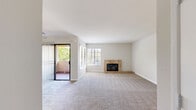 Located at 2371 Caringa Way in Carlsbad, CA, this single-floor residence offers two bedrooms, two bathrooms, and a well-organized layout that makes efficient use of its space. The living room serves as the centerpiece of the home, featuring plush carpeting, a tile-surround fireplace, and large windows paired with sliding glass door access to a private balcony, filling the area with natural light and outdoor views of the surrounding greenery. The kitchen is outfitted with white cabinetry, dark countertops, warm wood-look flooring, and a window above the sink that keeps the space bright and functional. Both bathrooms feature tub-shower combos with clean white tile surrounds and wood-look flooring. The primary bedroom is generously proportioned, highlighted by a wide picture window with outdoor views and a full wall of mirrored sliding closet doors that enhance the sense of space. The second bedroom is equally well-lit, with its own large window and built-in closet storage. A hallway connects the rooms efficiently, and a utility room adds practical convenience. Soft neutral tones and carpeting throughout the bedrooms and living areas contribute to a calm, cohesive ambiance well-suited to comfortable everyday living.