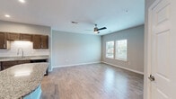 Located at 1910 E First St in Gulf Shores, Alabama, this single-story home offers a well-planned layout across a comfortable footprint. The open-concept design seamlessly connects the kitchen and living room, creating a bright and functional living area. Light wood-look flooring extends throughout the main living spaces, complemented by neutral gray walls and crisp white trim.

The kitchen is a standout feature, showcasing rich dark cabinetry, granite countertops, a classic subway tile backsplash, and a full suite of stainless steel appliances. A curved kitchen island provides additional counter space and casual seating, making it ideal for both cooking and entertaining. Recessed lighting illuminates the kitchen, while a ceiling fan adds comfort to the spacious living room, which receives natural light through double windows.

The bedroom is a peaceful retreat featuring plush carpet, a ceiling fan, a natural-light window, and access to a well-organized walk-in closet with built-in shelving. The bathroom offers granite countertops consistent with the home's design aesthetic. Additional practical spaces include a dedicated laundry area with washer/dryer hookups and overhead shelving, a pantry, a utility room, and a hallway connecting all areas efficiently.