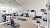 Located at 285 Park Ave in Pooler, Georgia, this fitness center offers a comprehensive and well-appointed workout facility on a single floor. The space is designed with a clean, modern aesthetic, featuring crisp white walls accented by crown molding and neutral-toned flooring throughout.

The main workout area is generously proportioned, bathed in natural light streaming through large arched windows and full-length glass doors that line the perimeter. Ceiling fans are strategically placed throughout to ensure comfortable airflow during workouts. Full-length wall mirrors visually expand the space and provide practical feedback for proper form.

The facility is equipped with an extensive array of strength training machines, including cable pull systems, leg press and extension machines, and multi-function resistance stations. A dedicated free weights section features a full rack of dumbbells alongside adjustable benches and exercise mats. The cardio zone includes treadmills, stationary bikes, and an elliptical trainer.

Motivational wall decals add an energetic and encouraging ambiance, while a mounted display screen provides entertainment or instructional content. A glass-enclosed entryway provides a clean transition into the space. The overall environment is bright, organized, and inviting, making it a well-rounded destination for a full-body fitness routine.