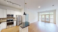 Located at 1114 Parktop Dr in Cary, NC, this single-floor residence offers a thoughtfully designed layout across two bedrooms and two bathrooms. The open-plan kitchen and living area serves as the heart of the home, featuring warm hardwood-style flooring that extends throughout. The kitchen is well-equipped with white shaker cabinetry, dark granite countertops, a textured tile backsplash, stainless steel appliances, and a striking hexagonal island with pendant lighting above — ideal for both meal preparation and casual dining. The living room is bright and airy, benefiting from a large set of French doors flanked by expansive windows that invite abundant natural light and offer views of the surrounding greenery. Both bedrooms continue the hardwood-style flooring and are fitted with ceiling fans and generous windows with outdoor views, creating a comfortable and well-lit atmosphere. The primary bedroom offers a notably spacious layout. Each bathroom is finished with dark granite vanity tops, undermount sinks, and warm-toned tile. One bathroom features a full soaking tub with tiled surround. Two closets and a hallway round out the functional floor plan, offering ample storage and easy circulation throughout the home.
