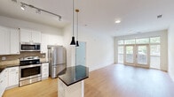 Located at 1114 Parktop Dr in Cary, NC, this single-floor residence offers a thoughtfully designed layout across two bedrooms and two bathrooms. The open-plan kitchen and living area serves as the heart of the home, featuring warm hardwood-style flooring that extends throughout. The kitchen is well-equipped with white shaker cabinetry, dark granite countertops, a textured tile backsplash, stainless steel appliances, and a striking hexagonal island with pendant lighting above — ideal for both meal preparation and casual dining. The living room is bright and airy, benefiting from a large set of French doors flanked by expansive windows that invite abundant natural light and offer views of the surrounding greenery. Both bedrooms continue the hardwood-style flooring and are fitted with ceiling fans and generous windows with outdoor views, creating a comfortable and well-lit atmosphere. The primary bedroom offers a notably spacious layout. Each bathroom is finished with dark granite vanity tops, undermount sinks, and warm-toned tile. One bathroom features a full soaking tub with tiled surround. Two closets and a hallway round out the functional floor plan, offering ample storage and easy circulation throughout the home.