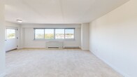 Located at 385 Ocean Blvd in Long Branch, NJ, this one-bedroom, one-bathroom unit offers a thoughtfully organized floor plan with comfortable living space spread across a single floor. The bright living area features wall-to-wall carpeting, crisp white walls, and a large multi-pane window that frames scenic outdoor views of the surrounding neighborhood, allowing abundant natural light to fill the room. A wall-mounted heating unit runs along the base of the window, providing efficient climate control.

The galley-style kitchen is neatly framed by structural columns and features warm wood cabinetry on both sides, dark granite-style countertops, tile flooring, and stainless steel appliances including a refrigerator, gas range, and sink — offering a functional and efficient cooking space.

The spacious primary bedroom accommodates generous furnishings and includes a large double-door closet as well as direct access to the hallway, providing a practical and private retreat. The full bathroom is finished with elegant floor-to-ceiling tiled walls in a neutral stone pattern accented by a decorative mosaic border, complementing the soaking tub and shower combination. A hallway and additional closet round out the layout, adding practical storage throughout this well-appointed coastal unit.