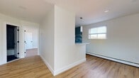 This single-floor unit has been thoughtfully renovated, blending contemporary finishes with a clean, functional layout. Light-toned hardwood-style flooring runs continuously throughout, unifying the space and complementing the bright, neutral walls.

The kitchen is a standout feature, anchored by bold teal herringbone-patterned tile backsplash that contrasts sharply with crisp white shaker cabinetry fitted with matte black hardware. Stainless steel appliances — including a refrigerator, gas range, and over-the-range microwave — complete the kitchen, which opens to the living area via a peninsula counter with a pendant light overhead. The open-plan design creates a seamless flow between kitchen and living spaces, both served by recessed lighting and baseboard heating.

The bedroom is a well-proportioned, quiet room with a window admitting natural light, and it connects directly to a walk-in closet with built-in shelving. The bathroom features a soaking tub framed by geometric patterned grey tile surround, dark floor tile, matte black fixtures, and a white vanity, offering a distinctly modern aesthetic throughout.