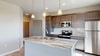 This single-floor residence offers a thoughtfully designed open-concept layout that seamlessly connects the living, dining, and kitchen areas. Light-toned luxury vinyl plank flooring runs throughout the main living spaces, complemented by neutral gray walls that create a clean, contemporary aesthetic. Large windows allow generous natural light to fill the space, offering pleasant outdoor views.

The kitchen serves as the centerpiece of the home, anchored by a substantial island topped with striking granite countertops featuring bold veining. Rich, dark-toned cabinetry provides ample storage, while a classic white subway tile backsplash adds a timeless contrast. A full suite of stainless steel appliances, including a range, microwave, and refrigerator, completes the kitchen. Pendant lighting above the island adds both function and visual appeal.

The living area benefits from a tray ceiling detail that adds architectural dimension, while a sliding door provides access to an outdoor space. Bedrooms are finished with plush carpeting and ceiling fans, and feature windows that bring in natural light.

The bathrooms are well-appointed, featuring granite-topped vanities with dark cabinetry that echo the kitchen's design. A combination tub and shower is present in one bathroom, while a second bathroom offers a double vanity. The overall ambiance is modern, clean, and move-in ready.