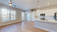 Located at Vieux at Welden in Kernersville, NC, this single-floor, 3-bedroom, 2-bathroom residence offers a thoughtfully designed open-concept layout with modern finishes throughout. The combined kitchen and living area serves as the heart of the home, featuring light hardwood-style flooring, neutral gray walls, and abundant natural light from multiple windows. A ceiling fan adds comfort to the living space, which also provides access to a private outdoor area.

The kitchen is a standout feature, boasting crisp white shaker cabinetry, a classic white subway tile backsplash, stainless steel appliances including a refrigerator, range, and microwave, and a large central island with a white quartz countertop and matte black sink faucet. Elegant glass pendant lights hang above the island, adding a polished finishing touch.

The primary bedroom offers generous proportions with plush carpeting, a ceiling fan, a large window with outdoor views, and a walk-in closet with wire shelving. The additional bedrooms are equally comfortable, each with carpet flooring and natural light. The bathrooms are clean and functional, featuring a soaking tub and shower combination with brushed nickel fixtures. Two closets provide ample storage throughout the residence.