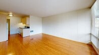 Located at 1905 NW 29th Ave in Portland, Oregon, this single-floor unit offers a well-organized and efficient layout that includes a combined kitchen and living area, a separate living room, a full bathroom, and two closets. The living spaces are unified by warm-toned bamboo hardwood flooring that runs throughout, complemented by clean white walls and a textured ceiling that enhances the sense of brightness. Large windows in the living room allow abundant natural light to fill the space, creating an open and airy atmosphere. The kitchen features light wood cabinetry, a dark countertop, a built-in sink, and a full-size refrigerator — all neatly arranged for practical everyday use. A full-wall paneled closet system in the living area provides ample built-in storage. The bathroom is finished with classic white subway tile in the tub/shower surround, accented by a dark tile border, and includes dark mosaic floor tiling. A private balcony extends the living space outdoors, overlooking a lush green lawn with mature trees and a wooded backdrop — a tranquil natural setting that adds significant character to this urban Portland residence.