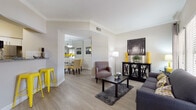 This single-story, 2-bedroom, 2-bathroom residence delivers a well-appointed living experience across a smartly organized floor plan. The open-concept living and dining area is finished with light wood-style flooring, crown molding, and neutral tones accented by bold pops of yellow throughout. Large windows allow generous natural light to fill the living room, which flows seamlessly into the dining area, complete with a pendant light fixture and mirrored accents. The kitchen features white cabinetry, granite-style countertops, a subway tile backsplash, stainless steel appliances including a range and dishwasher, and a pass-through bar area with seating. A full-size in-unit washer and dryer is a notable convenience. Both bedrooms offer plush carpeting, ceiling fans, and ample natural light through large windows with views of the surrounding greenery. Each bedroom includes generous closet space. The two bathrooms are finished with wood-style flooring and include tub-shower combinations with tile surrounds. The overall design balances comfort and practicality, creating a cohesive and welcoming living environment throughout.