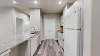 This single-story, one-bedroom, one-bathroom unit is located at 14441 T C Jester Boulevard in Houston, TX. The layout is efficiently designed, making excellent use of its footprint across a single floor. The open living area flows naturally toward the kitchen, which serves as a standout feature of the space. Finished with crisp white cabinetry extending to the ceiling, granite countertops, a subway tile backsplash, and a full suite of white appliances including a refrigerator, range, microwave, and dishwasher, the kitchen is both functional and visually cohesive. A peninsula counter with granite surface provides additional workspace and separation between the kitchen and living area. Wood-look plank flooring runs throughout the main living areas, adding warmth and continuity, while recessed lighting and neutral gray-toned walls keep the space feeling clean and modern. The bedroom is generously sized, featuring plush carpet, a ceiling fan, a window with natural light, and a closet. The bathroom is well-appointed with a granite-topped vanity, white cabinetry, a large mirror, and a tub-shower combination clad in classic white subway tile. A dedicated utility room adds practical storage and functionality. The overall aesthetic is modern and neutral throughout.