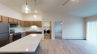 This single-floor residence offers a thoughtfully designed open-concept layout with light hardwood-style flooring throughout the main living areas. The kitchen serves as a central hub, featuring warm medium-toned shaker-style cabinetry, white quartz countertops, a stainless steel appliance suite including a refrigerator, range, microwave, and dishwasher, and a central island with a contrasting blue base. Pendant lighting above the island adds a refined touch. The kitchen also includes an undermount sink with under-cabinet lighting along the perimeter counters.

A dedicated laundry room is conveniently accessible from the main living area and houses a full-sized front-loading washer and dryer with overhead shelving. The bedrooms are carpeted and each equipped with a ceiling fan, baseboard heating, and windows that allow natural light. One bedroom features a walk-in closet with built-in shelving and a bench.

Two bathrooms serve the unit: one with a soaking tub and dark vanity cabinetry with a white countertop, and another with a walk-in shower, dark cabinetry, and continued hardwood-style flooring. The overall aesthetic is clean and modern with neutral tones throughout.
