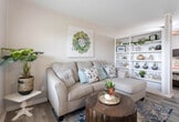Located at 5301 11th St in Lubbock, Texas, this single-floor home offers a thoughtfully arranged and warmly styled living space. The open-concept layout seamlessly connects the living area to the sleeping space, separated by a charming built-in white shelving unit that serves as both a functional divider and an attractive display feature. The living area is anchored by light hardwood-style flooring and neutral-toned walls, creating a bright and welcoming ambiance. A comfortable sectional sofa and decorative accents give the space a cozy, lived-in feel.

The sleeping area, partially open to the living space via the shelving partition, is framed by vertical wood-paneled walls and receives natural light through a nearby window, lending it a calm and restful atmosphere.

The kitchen is well-equipped with white cabinetry, a full-size refrigerator, an electric range, and ample counter space with a gray laminate finish. A peninsula-style counter adds additional workspace and casual dining potential.

The bathroom is clean and simply appointed, featuring a white vanity, neutral gray walls, and the same hardwood-style flooring found throughout the home, maintaining a cohesive aesthetic. Together, the rooms offer a compact yet complete and functional living environment with consistent, understated charm.