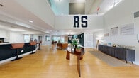 Located at 3250 Mercer University Dr in Chamblee, GA, this two-floor commercial space offers a thoughtfully designed layout spanning a generous total area across both levels. The ground floor houses a well-equipped fitness center with rubber flooring, a multi-station cable machine, a stationary bike, treadmill, and a wall-mounted TV — all benefiting from natural light through large windows overlooking greenery outside. Two ADA-accessible bathrooms with grab bars and tile flooring serve the space conveniently. A welcoming hallway with vaulted ceilings and warm hardwood flooring connects areas seamlessly. The kitchen features crisp white shaker cabinetry, dark granite countertops, a teal accent wall, and stainless steel appliances, providing a fully functional prep area. The upper floor expands the space considerably, highlighted by a stylish living room with soaring ceilings, a white fireplace framed by deep green accent walls, a statement chandelier, and hardwood floors. A formal conference/dining room accommodates a large walnut table with black leather seating and a wall-mounted display, ideal for meetings or gatherings. An additional private office with a pass-through window completes the upper level, creating a versatile, multi-purpose environment throughout.