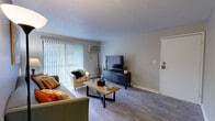 This 2-bedroom, 2-bathroom residence is thoughtfully laid out across a single floor, making efficient use of its space while maintaining a comfortable and functional living environment. Light gray walls and wood-style laminate flooring run throughout, creating a cohesive and contemporary aesthetic.

The living room serves as the heart of the home, featuring a large sliding glass door framed by vertical blinds that fills the space with natural light and provides access to the outdoors. A wall-mounted air conditioning unit ensures year-round comfort. The kitchen is designed in a classic galley style, featuring white cabinetry with modern hardware, light countertops, a stainless steel sink, and black appliances including a full-size refrigerator, range, and dishwasher.

The primary bedroom offers a generous footprint with a sliding-door closet providing ample storage. The second bedroom is well-sized and includes a window with blinds, offering natural light and a quiet retreat. A hallway connects the living areas to the bedrooms and bathrooms, with one full bathroom featuring a shower and a second bathroom with a white vanity, framed mirror, and clean, neutral finishes. An additional closet provides supplementary storage, completing this efficiently designed and move-in-ready home.