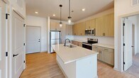 Located at 2427–2443 Wilkinson Blvd in Charlotte, NC, this well-appointed 2-bedroom, 2-bathroom unit offers a thoughtfully designed single-floor layout with modern finishes throughout. The kitchen serves as a standout centerpiece, featuring light wood shaker-style cabinetry, quartz countertops, a large island with an undermount sink, stainless steel appliances including a refrigerator, range, and microwave, and elegant pendant lighting above the island. Light wood-look flooring grounds the kitchen and entry area, adding warmth and continuity. Both bedrooms are carpeted and filled with natural light through large windows fitted with blinds, offering views of the surrounding Charlotte skyline. Ceiling fans are installed in each bedroom for added comfort. The primary bedroom includes dedicated closet space and direct access to its private bathroom, which features a dual-sink vanity with quartz countertops, wood-tone cabinetry, and matte black fixtures. The second bathroom is equipped with a full tub-shower combination with tiled surround. Built-in shelving adds functional storage in the primary bedroom area. The overall aesthetic is clean and contemporary, with neutral tones, recessed lighting, and cohesive design elements creating a bright, inviting atmosphere throughout.