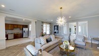Located at 28013 Hwy 181 in Daphne, Alabama, this single-story home offers a thoughtfully designed interior that blends elegance with everyday comfort. The open-concept living area serves as the heart of the home, featuring light gray walls accented by crisp crown molding and decorative columns that define the space without sacrificing its open feel. A striking coral-shaped chandelier with a brass finish serves as a focal centerpiece, casting warm light across the room. Natural light filters in through multiple windows dressed with patterned drapes, enhancing the airy atmosphere. The living area flows seamlessly into the dining space and kitchen, which is equipped with stainless steel appliances including a French door refrigerator and rich dark wood cabinetry. Light hardwood-style flooring runs throughout, tying the spaces together cohesively. The dining area continues the refined aesthetic with coordinating upholstered seating. Neutral tones, layered textiles, and coastal-inspired accents contribute to a sophisticated yet approachable ambiance. This home offers a polished, move-in-ready interior designed for both style and functionality.
