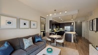This thoughtfully designed single-floor residence offers a seamless open-concept layout that connects the living, dining, and kitchen areas into one cohesive and functional space. The living area features warm neutral tones, track lighting, and a large floor-length mirror that enhances the sense of openness. Framed wall art adds a refined, contemporary touch throughout.

The gourmet kitchen is a standout feature, showcasing rich espresso-toned cabinetry that extends to the ceiling, a striking mosaic tile backsplash, and light granite countertops that continue onto a generously sized island with seating. Stainless steel appliances — including a gas range, built-in microwave, dishwasher, and French door refrigerator — complement the modern aesthetic. Elegant pendant lighting illuminates the island, adding warmth and style. Hardwood-style flooring flows throughout the main living areas.

The bedroom is a serene retreat, bathed in natural light through large windows that offer views of lush landscaping. Neutral carpet, floor-length curtains, and roller shades provide comfort and privacy.

The bathroom is finished with matching granite vanity surfaces and dark cabinetry, and includes a soaking tub with shower. A glass-panel door leads directly into a spacious walk-in closet, adding practical storage to complete this well-appointed residence.