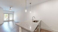 This well-appointed single-floor unit offers a thoughtfully designed open-concept layout, seamlessly connecting the kitchen, dining, and living areas. The kitchen serves as a central hub, featuring a granite-topped island with an integrated sink and stylish pendant lighting suspended above. Grey shaker-style cabinetry, a subway tile backsplash, granite countertops, and stainless steel appliances — including a refrigerator and built-in microwave — complete the space with a clean, contemporary aesthetic. Hardwood-style flooring extends throughout the unit, lending warmth and visual continuity across every room. The living area is bright and open, benefiting from natural light and providing access to a private patio through double glass doors. The bedrooms are generously proportioned, each featuring ceiling fans, large windows with blinds, and access to well-organized closet space. The bathroom is finished with grey subway tile surrounding the soaking tub and shower, a granite vanity with grey cabinetry, and coordinating brushed nickel fixtures. Throughout, the unit maintains a neutral, modern palette with crisp white walls and consistent finishes, creating a cohesive and inviting living environment.