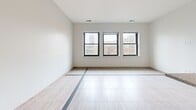 Located at 1145 Griswold in the heart of downtown Detroit, this one-bedroom, one-bathroom residence offers a well-designed layout across a single floor. The open living area features large tile flooring with a distinctive inlaid accent border, neutral wall tones, and a trio of black-framed windows that frame dynamic views of Detroit's iconic skyline and neighboring architecture, filling the space with natural light.

The kitchen is a standout feature, showcasing rich dark mahogany cabinetry, granite countertops, and a spacious island with pendant lighting overhead. Stainless steel appliances — including a gas range, microwave, dishwasher, and refrigerator — complete this functional and stylish culinary space. Light wood-tone flooring flows seamlessly through the kitchen and living areas.

The bedroom is carpeted for comfort and offers a quiet retreat, connecting to the rest of the unit through a clean, well-lit hallway. The bathroom is finished with tile flooring, a glass-enclosed shower, and a clean, minimalist aesthetic consistent with the rest of the home.

Throughout the unit, the design reflects a modern urban sensibility — clean lines, quality finishes, and a neutral palette that provides an ideal backdrop for city living in one of Detroit's most vibrant downtown locations.
