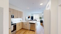 This well-designed single-floor unit offers a thoughtful layout that maximizes its compact footprint across four distinct spaces. The open-concept kitchen and living area form the heart of the unit, where light wood cabinetry, white quartz countertops, and a classic subway tile backsplash lend a clean, contemporary aesthetic to the kitchen. Stainless steel appliances—including a refrigerator, range, microwave, and dishwasher—provide a full suite of modern conveniences, while a peninsula counter creates a natural transition into the living area. The living space is bright and airy, benefiting from a large window that draws in natural light and offers views of the surrounding neighborhood. Warm-toned hardwood flooring runs continuously throughout, unifying the open layout. The bedroom is a serene retreat, featuring its own oversized window with street-level views, crisp white walls, and ample room for furnishings. The bathroom is finished in a minimalist style with white subway tile in the walk-in shower, a wood-toned vanity with an undermount sink, and coordinating hardwood flooring. Clean lines, neutral tones, and quality finishes give the entire space a cohesive and modern character.