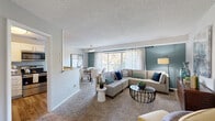 This single-floor residence offers a thoughtfully designed layout that balances comfort and functionality. The open-concept living and dining area is anchored by plush carpeting, a textured ceiling, and a calming teal accent wall that adds a touch of warmth and character. A large sliding glass door floods the space with natural light and provides direct access to a private balcony overlooking lush greenery — an ideal setting for relaxing outdoors. Sheer curtains frame the expansive windows, enhancing the airy ambiance throughout.

The kitchen is well-equipped with stainless steel appliances including a refrigerator, dishwasher, electric range, and over-the-range microwave. White shaker-style cabinetry pairs cleanly with granite countertops and a soft blue subway tile backsplash, while wood-look flooring grounds the space with a contemporary feel. A pass-through window connects the kitchen to the dining area, promoting an open flow ideal for entertaining.

The bedroom is generously sized with plush carpet, ample closet storage, and convenient in-unit laundry access visible through the hallway. The bathroom features granite countertops, a full tub-shower combination, wood-look flooring, and clean white cabinetry. The entry area provides a welcoming transition into the living space, completing this well-rounded residence.
