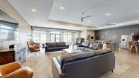 Located at 600 NW Cherrycreek Ln in Ankeny, Iowa, this single-floor community clubhouse delivers a well-appointed, open-concept layout that seamlessly blends modern and industrial design aesthetics. Polished concrete floors extend throughout the entire space, creating a cohesive and easy-to-maintain foundation that complements the overall style.

The expansive living area is anchored by comfortable leather seating arrangements, wood-accented coffee tables, and a large wall-mounted flat-screen TV set against a textured concrete block wall. Oversized windows along the exterior walls flood the space with generous natural light and offer views of the surrounding community. A ceiling fan adds to the comfort of the room, and recessed lighting ensures a bright atmosphere after dark. Glass-paneled room dividers near the entrance provide flexible, semi-private spaces for smaller gatherings.

The kitchen features rich, dark wood cabinetry paired with light quartz countertops and a large central island clad in reclaimed wood paneling. Industrial-style metal barstools line the island, making it an ideal spot for casual dining or socializing. Stainless steel appliances, including a refrigerator and microwave, complete the functional yet stylish kitchen setup. Together, these spaces form a welcoming and versatile communal environment suited for a variety of social activities.