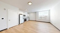 Located at 222 Canal St in New Haven, CT, this single-floor unit offers a clean, modern design with a highly functional open layout. The combined kitchen and living area forms the heart of the space, bathed in natural light from a large window that frames views of the surrounding New Haven cityscape. Light hardwood flooring runs continuously throughout, lending warmth and visual continuity to the interior.

The kitchen is well-appointed with crisp white shaker-style cabinetry, granite countertops, and a full suite of stainless steel appliances, including a refrigerator, range, over-the-range microwave, and dishwasher. Open shelving accents the upper cabinetry, adding a contemporary touch. Flush-mount ceiling fixtures provide consistent ambient lighting across the open living area, which offers a generous, flexible space well-suited for various furniture arrangements.

The bathroom is finished in a neutral, modern palette featuring large-format tile flooring, a walk-in shower with built-in corner shelving, a vanity with a white quartz countertop and undermount sink, and a wide mirror with overhead lighting. Throughout the unit, the clean white walls and minimalist finishes create a bright, cohesive ambiance that reflects a contemporary urban aesthetic.