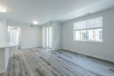 This single-floor unit presents a clean, contemporary design highlighted by light-toned wood-style flooring that runs consistently throughout the space, creating a cohesive and airy feel. The open living area benefits from natural light streaming through windows fitted with horizontal blinds, and a set of sliding glass-paned doors adds an elegant touch while connecting to an adjacent room or hallway.

The kitchen is well-equipped with a full suite of stainless steel appliances, including a gas range, over-the-range microwave, dishwasher, and refrigerator. White flat-front cabinetry with matte black hardware pairs with dark countertops to deliver a sharp, modern contrast, while recessed lighting and a window above the sink keep the space bright and functional.

Two bathrooms mirror each other in style, each featuring a tub-shower combination with white tile surround, a white vanity with a dark countertop, and a window for natural ventilation and light. The bedrooms are well-proportioned with large windows and neutral walls. One bedroom includes a walk-in closet outfitted with a hanging rod and built-in shelving unit, providing practical, organized storage. Overall, the unit exudes a fresh, move-in-ready quality throughout.
