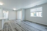 This single-floor unit presents a clean, contemporary design highlighted by light-toned wood-style flooring that runs consistently throughout the space, creating a cohesive and airy feel. The open living area benefits from natural light streaming through windows fitted with horizontal blinds, and a set of sliding glass-paned doors adds an elegant touch while connecting to an adjacent room or hallway.

The kitchen is well-equipped with a full suite of stainless steel appliances, including a gas range, over-the-range microwave, dishwasher, and refrigerator. White flat-front cabinetry with matte black hardware pairs with dark countertops to deliver a sharp, modern contrast, while recessed lighting and a window above the sink keep the space bright and functional.

Two bathrooms mirror each other in style, each featuring a tub-shower combination with white tile surround, a white vanity with a dark countertop, and a window for natural ventilation and light. The bedrooms are well-proportioned with large windows and neutral walls. One bedroom includes a walk-in closet outfitted with a hanging rod and built-in shelving unit, providing practical, organized storage. Overall, the unit exudes a fresh, move-in-ready quality throughout.