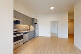 Located at 636 W 6th St in Vancouver, WA, this efficiently designed four-bedroom, one-bathroom unit offers a clean, modern aesthetic throughout. Light wood-tone luxury vinyl plank flooring runs continuously across all rooms, creating a bright and cohesive look. The open kitchen is outfitted with gray cabinetry, a tile backsplash, stainless steel appliances including a range, dishwasher, and refrigerator, and flows naturally into the living area. A hallway connects the living space to the four bedrooms, each featuring white walls, large black-framed windows that bring in natural light and urban views of the Vancouver skyline and surrounding development. The primary bedroom provides a comfortable, well-proportioned retreat. The shared bathroom is clean and contemporary, featuring a full soaking tub with a tiled surround and chrome fixtures. A standout convenience of this unit is the in-unit stacked Whirlpool washer and dryer, neatly tucked into a hallway closet. Black-framed floor-to-ceiling windows and a glass door in the living area provide sweeping city views and access to the outdoors, lending the space an airy, connected feel within its urban setting.