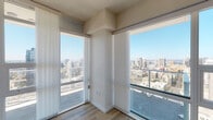 Located in the heart of downtown San Diego at 1150 E Street, this modern high-rise unit offers a sleek, contemporary living experience with stunning panoramic views of the city skyline. The open living area is defined by expansive floor-to-ceiling windows and sliding glass doors that flood the space with natural light and frame sweeping vistas of the San Diego cityscape. Light wood-tone flooring runs throughout, complementing the clean, neutral palette of the interiors.

The kitchen is outfitted with modern gray cabinetry, white quartz countertops, stainless steel appliances including a French door refrigerator, built-in microwave, and dishwasher, creating a functional and stylish culinary space. The galley-style layout maximizes efficiency while maintaining an open connection to the rest of the unit.

The bedrooms continue the theme of abundant natural light, each featuring large windows with commanding city views, providing an airy and elevated atmosphere. The bathrooms are finished with marble-tiled tub and shower surrounds, white quartz vanity tops, gray cabinetry, and large framed mirrors, offering a clean and refined aesthetic. The overall design emphasizes openness, light, and modern urban living with high-quality finishes throughout.
