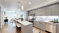This thoughtfully designed 2-bedroom, 2-bathroom single-floor residence offers a modern aesthetic with clean lines and contemporary finishes throughout. The open-concept kitchen and living area serves as the heart of the home, featuring a sleek kitchen equipped with gray flat-front cabinetry, stainless steel appliances including a gas range, built-in microwave, dishwasher, and refrigerator, complemented by white quartz countertops and a subway tile backsplash. A central island with seating provides additional prep space and a casual dining option. The adjacent living room is bright and welcoming, with large windows and glass doors that invite abundant natural light and outdoor views, along with light hardwood-style flooring and a ceiling fan overhead. Both bedrooms are generously proportioned, carpeted for comfort, and feature ceiling fans and windows with outdoor views. The primary bedroom includes a spacious walk-in closet with built-in shelving and organizational systems. The primary bathroom offers a dual-sink vanity with gray cabinetry, large-format tile flooring, and a bathtub/shower combination, while the second bathroom features a single floating vanity and tiled floors. Two dedicated closets contribute to ample overall storage throughout the residence.