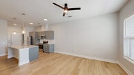 This single-floor, two-bedroom, two-bathroom unit offers a well-designed layout with modern finishes throughout. The open-concept living and kitchen area forms the heart of the space, anchored by light-toned hardwood-style flooring and neutral gray walls. A ceiling fan with integrated lighting serves both the kitchen and living zone, while recessed lighting and pendant fixtures over the island add focused illumination.

The kitchen is a standout feature, equipped with gray shaker-style cabinetry extending to near ceiling height for ample storage, a white subway tile backsplash, granite-look countertops, and a full suite of stainless steel appliances including a refrigerator, range, and microwave. A central island with a sink and additional seating space enhances both functionality and flow.

The living area benefits from natural light through windows and a glass door leading outside. Both bedrooms feature plush carpeting and closets with wire shelving. The two bathrooms mirror the kitchen's aesthetic, featuring gray vanities with granite-look countertops and tile flooring. One bathroom includes a tub-shower combination with white tile surround, completing a cohesive, contemporary design throughout the unit.