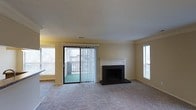 Located at 601 Jones Ferry Rd in Carrboro, North Carolina, this single-floor residence offers a comfortable and well-appointed living environment. The main living area is a standout feature of the home, finished with plush wall-to-wall carpeting that adds warmth underfoot. Crown molding lines the ceiling, lending a refined architectural detail to the space, while a textured ceiling adds subtle character overhead. A classic fireplace with a crisp white mantel and dark brick surround serves as a focal point, providing both aesthetic appeal and functional comfort. Natural light flows generously into the room through multiple windows fitted with blinds, as well as a sliding glass door that opens to a private balcony — ideal for enjoying outdoor views. The vertical blinds on the sliding door offer privacy and light control as needed. The warm yellow-toned walls create an inviting, neutral atmosphere throughout. The layout is open and spacious, allowing for flexible furniture arrangements. Overall, the space strikes a balance between classic design elements and everyday practicality, making it a welcoming and functional home in the heart of Carrboro.