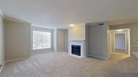 This contemporary apartment showcases an open-concept design, seamlessly blending living and dining areas. The focal point is a classic white fireplace, adding warmth and character. The updated kitchen boasts stainless steel appliances, white cabinetry, and a convenient breakfast bar. Large windows allow ample natural light, enhancing the neutral color palette. Plush carpeting in main areas offers comfort, while the bathroom features modern fixtures and wood-look flooring. The bedroom is spacious and bright, with multiple windows. Overall, the space offers a harmonious blend of modern amenities and cozy living.