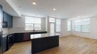Located near I-435 N in Lenexa, Kansas, this single-floor residence offers a contemporary and well-designed living environment. The open-concept kitchen serves as a central highlight, showcasing deep teal cabinetry, granite countertops, a subway tile backsplash, and a full suite of stainless steel appliances including a French door refrigerator, range, microwave, and dishwasher. A large center island with matching granite provides additional prep and seating space, while wide windows flood the area with natural light and offer outdoor views. Light hardwood flooring runs throughout the main living and kitchen areas, contributing to a warm and cohesive aesthetic. The bedrooms are generously sized, featuring plush carpeting, ceiling fans, and windows that bring in ample daylight. One room features hardwood flooring and connects to a spacious walk-in closet outfitted with built-in wooden shelving and hanging rods. The bathroom is finished to a high standard, with a granite-topped vanity, backlit mirror, a glass-enclosed walk-in shower with full tile surround, and hardwood flooring. Clean white walls and consistent modern finishes throughout the space create a bright, move-in-ready atmosphere.