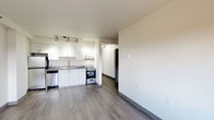 Located on the 10th floor at 29 St. Helens Avenue in Tacoma, WA, Unit 1005 is a well-designed single-floor residence that balances functionality with a clean, modern aesthetic. The open-concept layout connects the living area to the kitchen, creating an airy and cohesive living space. Durable wood-look laminate flooring runs throughout the main living and kitchen areas, lending a contemporary feel.

The kitchen is efficiently appointed with crisp white cabinetry — both upper and lower — complemented by dark countertops and a double stainless steel sink. A stainless steel refrigerator, electric range, and dishwasher complete the fully equipped setup, while track lighting overhead ensures ample illumination for meal prep.

The living area is bright and open, highlighted by a large window that frames lush outdoor greenery, filling the space with natural light. A baseboard heating system provides consistent warmth throughout. The bedroom features plush carpeting and its own window with the same pleasant outdoor views, offering a quiet and comfortable retreat.

The bathroom is neatly finished with a vanity featuring dark countertops and modern hardware, a full tub/shower combo with a curved curtain rod, and tile-style flooring. The overall design of the unit is clean and neutral, offering a versatile canvas for personalization.