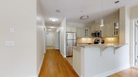 This thoughtfully designed single-floor residence offers a generous footprint spread across one level, featuring one bedroom, three bathrooms, and a seamless open layout. Two entrance points provide convenient access, leading into a welcoming hallway finished with warm hardwood flooring that extends throughout the main living areas.

The combined kitchen and living room forms the heart of the home. The kitchen is well-equipped with stainless steel appliances, including a refrigerator, range, and built-in microwave, complemented by cream-toned cabinetry with glass-front uppers, granite countertops, and a breakfast bar peninsula. The kitchen transitions into the living area, which features a tile-surround fireplace, arched windows, and access to an outdoor balcony overlooking a landscaped courtyard with mature trees.

The bedroom is a calm, neutral space with hardwood floors, built-in closets, and an adjacent hallway leading to additional storage. The three bathrooms are consistently finished with granite-topped vanities, cream cabinetry, chrome fixtures, and tile flooring, with at least one featuring a full tub-shower combination. The overall aesthetic is clean and cohesive throughout.