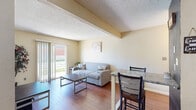 This single-floor unit in Montgomery, Indiana, offers a straightforward and functional layout designed for comfortable everyday living. The living area serves as the central gathering space, featuring warm hardwood-style flooring, neutral beige walls, and a textured ceiling. A sliding glass door floods the room with natural light and provides views of the outdoors, while an adjacent bar-height dining area offers a convenient spot for casual meals.

The kitchen is well-equipped with white cabinetry providing ample storage, granite-style countertops, and black appliances including a full-size refrigerator, electric range with overhead ventilation, and microwave. The warm-toned accent walls add a distinctive character to the space, complementing the hardwood-style flooring that continues from the living area.

Multiple bedrooms are carpeted and finished in soft neutral tones, each offering a calm and restful atmosphere. Natural light filters in through window blinds, and at least one bedroom includes a dedicated closet with built-in shelving for organized storage.

The bathroom features tile flooring, a wall-mounted storage cabinet, and clean, accessible fixtures in a bright, neutral setting. Overall, the unit presents a practical and cohesive living environment with consistent finishes throughout.