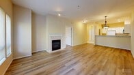 Located at 12224 NE 8th St in Bellevue, WA, this well-appointed two-bedroom, two-bathroom residence offers a thoughtfully designed single-floor layout with a comfortable, functional flow. The open-concept living room is a standout, featuring warm hardwood-style flooring, a tile-surround fireplace with a classic white mantle, and large windows that flood the space with natural light while offering lush, tree-lined views. A glass door leads to a private balcony, extending the living area outdoors. The adjacent kitchen is well-equipped with white cabinetry, a stainless steel microwave, white appliances including a range and dishwasher, and light tile flooring. A raised breakfast bar provides a seamless transition between the kitchen and living areas. The spacious primary bedroom includes ample closet space, while both bedrooms benefit from large windows with garden views and hardwood-style flooring. The primary bathroom features a dual-sink vanity with dark countertops, white cabinetry, and a tub/shower combo. The second bathroom offers a single vanity with a similarly clean, neutral aesthetic. Additional highlights include five closets providing generous storage, an in-unit laundry area, and recessed lighting throughout.