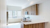 This well-designed multi-floor home offers four bedrooms, two bathrooms, and a thoughtfully arranged layout spread across three levels. The ground floor includes an attached garage with ample space and utility access, alongside additional storage areas. A carpeted staircase with a sleek metal railing connects the levels, providing a clean transition between floors. The main living level features a combined kitchen and living area bathed in natural light from large windows. The kitchen is appointed with warm wood-toned cabinetry extending to the ceiling, white quartz countertops, stainless steel appliances including a built-in microwave, electric range, dishwasher, and refrigerator, and a peninsula with a double undermount sink — a functional and stylish centerpiece. Light hardwood flooring flows throughout the main living spaces, enhancing the bright, contemporary ambiance. The bathrooms feature crisp white subway-tiled tub-shower combinations with modern matte black fixtures and accented tile flooring. The generously sized primary bedroom, the largest of the four, opens directly onto a private balcony through sliding glass doors, offering outdoor views of surrounding greenery. Recessed lighting throughout maintains a clean, modern aesthetic across the entire home.