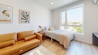 Located at 355 Glendale Blvd in the vibrant Echo Park neighborhood of Los Angeles, this thoughtfully designed one-bedroom, one-bathroom unit makes excellent use of its compact footprint across a single floor. The open layout connects the main living area to a well-appointed kitchen, which serves as a visual highlight with its striking deep-blue subway tile backsplash, sleek quartz countertops, matte black fixtures, stainless steel undermount sink, and integrated dishwasher. White upper cabinetry and light wood lower cabinets complete the modern aesthetic. The bedroom is a bright, comfortable retreat featuring light hardwood-style flooring, crisp white walls, and a large picture window that floods the space with natural light and offers open city views. The bathroom is clean and contemporary, finished with large-format white floor tiles, a floating vanity with an oversized mirror, white subway tile in the shower, and a curtained tub-shower combination. A standout practical feature is the in-unit stacked washer and dryer, neatly tucked into a dedicated closet alcove off the main living area. Light wood flooring flows throughout, tying the space together with warmth and cohesion.