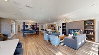 Located at 3010 Furr Court in Charlotte, NC, this thoughtfully designed single-floor community space offers a generous, open-plan interior that seamlessly blends social and recreational functions. Wide-plank hardwood-style flooring flows throughout, unifying each distinct zone beneath a bright, recessed-lit ceiling.

The kitchen area serves as a functional hub, featuring a long white quartz peninsula with bar-height seating, a stainless steel refrigerator, and a striking stacked-stone accent wall. Pendant lighting in brass finishes adds warmth and a refined touch.

The main living area is anchored by a built-in fireplace framed by a wood-panel surround and flanked by open shelving. Plush gray sofas and curved blue velvet accent chairs are arranged atop a bold striped area rug, creating an inviting lounge setting. A sculptural chandelier adds an artistic focal point overhead.

A dedicated billiards zone features a full-size pool table positioned between bold navy accent columns and a wall-mounted TV, lending an energetic, game-room atmosphere.

Toward the rear, an intimate seating nook with textured wallcovering and wall sconces looks out through large windows onto a resort-style pool. French doors provide direct outdoor access, flooding the space with natural light and views of the surrounding amenity deck.