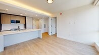 Located at 205 E 110th St in East Harlem, New York, this thoughtfully designed one-bedroom, one-bathroom residence offers a clean, contemporary aesthetic throughout. Light-toned hardwood flooring flows seamlessly across the entire unit, creating a warm and cohesive feel from room to room.

The open-concept living and kitchen area is anchored by a sleek kitchen island with a white countertop, complemented by modern cabinetry in light wood tones and a built-in microwave. Recessed and cove lighting adds a refined ambiance to the space. An entry hallway provides a practical transition into the living area.

The bedroom is bright and airy, featuring large black-framed windows that invite abundant natural light and offer open views of the surrounding New York City skyline and neighborhood rooftops. A double-door closet provides convenient storage within the room.

The bathroom is a standout feature, finished with large-format marble-style wall tiles in white and grey tones. A soaking tub with matte black fixtures and a handheld showerhead adds both style and function, while warm wood-toned cabinetry below the vanity echoes the unit's modern design language.

Overall, the unit presents a fresh, minimalist interior with high-quality finishes, making it a refined urban residence in the heart of New York City.