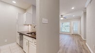 This single-story, 2-bedroom, 1-bathroom residence offers a thoughtfully designed layout with a clean, modern aesthetic throughout. The combined kitchen and living area forms the heart of the home, where the kitchen features white cabinetry, dark granite countertops, a tile backsplash, stainless steel appliances including a refrigerator and dishwasher, and tile flooring. The adjacent living area is bright and welcoming, benefiting from large windows that allow abundant natural light and direct access to the outdoors via a glass-paneled door. A ceiling fan adds both comfort and style to the space. Crown molding accents the living area, lending an elevated finish. Light wood-look flooring flows throughout the main living spaces and bedrooms, creating a cohesive and contemporary look. The primary bedroom is generously sized, featuring large windows with outdoor views and a ceiling fan. The second bedroom includes built-in shelving, crown molding, and the same warm wood-look floors. A light-filled hallway connects the bedrooms to the full bathroom, which is equipped with a wide vanity, dark granite countertop, a large mirror, and a tub-shower combination. An in-unit stacked washer and dryer is also conveniently located within the home.