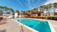 Located at 5100 Highpoint Rd in Union City, Georgia, this outdoor amenity space centers around a generously sized rectangular swimming pool set within a well-defined pool deck. The pool area is enclosed by a sturdy iron security fence, providing a secure and private environment for residents. The surrounding concrete sundeck offers ample space for relaxation, furnished with vibrant red lounge chairs positioned along the perimeter of the pool.

A gabled clubhouse or amenity building is situated directly adjacent to the pool area, featuring large windows and a welcoming entrance, and serves as a functional support structure for the pool facility. A covered pergola-style structure adds an additional shaded gathering spot near the pool deck.

Manicured hedges and well-maintained landscaping line the pool enclosure, contributing to a clean and organized aesthetic. Tall pine trees form a natural backdrop that surrounds the entire area, offering a sense of seclusion and a connection to the natural environment. The open-sky setting allows for abundant natural light throughout the day.

The pool itself is clearly marked with depth indicators and a "No Diving" sign, reflecting attention to safety. The overall layout is thoughtfully designed to serve as a community leisure destination, balancing functionality with an inviting outdoor atmosphere ideal for warm Georgia days.