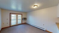 This single-floor unit offers a practical and straightforward layout designed for comfortable everyday living. The open-concept living area is finished with neutral-toned wall-to-wall carpeting and features a textured ceiling with flush-mount lighting. A baseboard heating system runs along the exterior wall, and a wall-mounted air conditioning unit provides year-round climate control. Double glass doors lead to a private balcony, allowing natural light to fill the space and providing outdoor views.

The kitchen is thoughtfully designed with a pass-through counter that connects it to the main living area, creating an open and accessible feel. It is equipped with warm-toned wood cabinetry, light speckled countertops, a built-in dishwasher, an electric range, and a sink. Wood-look flooring in the kitchen adds a clean contrast to the carpeted living spaces.

The bedroom is a well-proportioned, carpeted room with a large window that brings in natural light, a baseboard heater, and direct access through a wood-paneled door. The bathroom includes a white vanity with storage, a toilet, and a full tub and shower combination fitted with a grab bar for added accessibility. Wood-look flooring completes the bathroom's clean, functional finish.