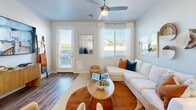 Located at 8450 S 59th Ave in Phoenix, AZ, this well-appointed single-story home offers three bedrooms and three full bathrooms across a thoughtfully designed floor plan. The open-concept kitchen and living area serves as the heart of the home, featuring white shaker cabinetry, white quartz countertops, stainless steel appliances including a refrigerator, range, microwave, and dishwasher, and a breakfast bar peninsula with seating. Wood-look flooring runs throughout, adding warmth and continuity to the space. The living room is bright and welcoming, with multiple windows that invite natural light and provide outdoor views, complemented by a ceiling fan overhead and direct access to the exterior. The primary bedroom is generously sized and includes an en-suite bathroom with a dual-sink vanity, white cabinetry, and a large mirror, as well as a dedicated walk-in closet with built-in shelving and hanging rods. The additional bedrooms are well-proportioned, each with ceiling fans and ample natural light. Secondary bathrooms feature clean white finishes, with one including a shower-tub combo. Hallways connect the rooms efficiently, and the overall design presents a clean, modern aesthetic with a neutral color palette throughout.